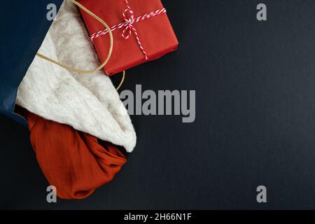 Shopping bag with clothes and gift on black background. Copy space. Top view. Stock Photo