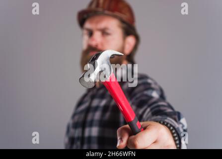 Worker, Carpenter or builder in hard hat with hammer. Selective focus. Bearded man in helmet hammering nail. Stock Photo
