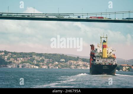 urban scene of the Bosphorus Strait with a cargo ship crossing the bridge busy with vehicles in a row, Turkey Stock Photo