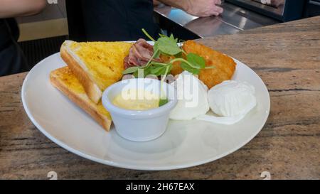A meal of poached eggs, bacon, fish, toast and sauce serve on a large white place and topped with greens Stock Photo
