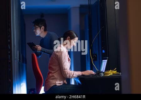Caucasian female engineer using laptop and asian male engineer inspecting in computer server room Stock Photo