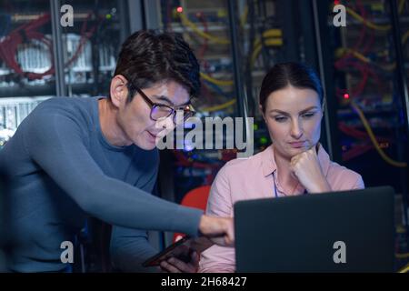 Diverse male and female engineers discussing over a laptop in computer server room Stock Photo
