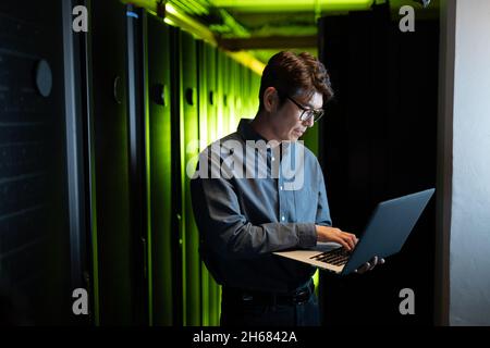 Asian male engineer using laptop in computer server room Stock Photo