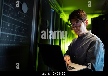 Asian male engineer using laptop in computer server room Stock Photo
