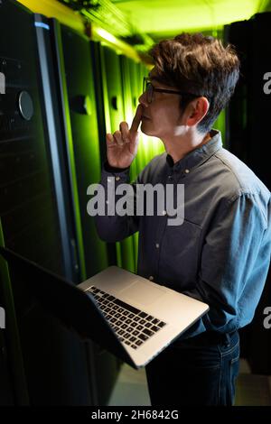 Thoughtful asian male engineer with laptop inspecting in computer server room Stock Photo