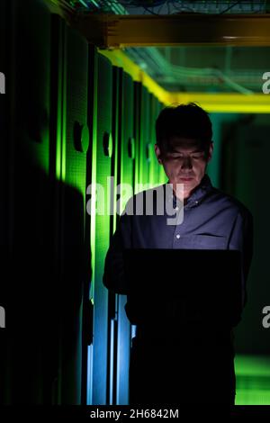 Asian male engineer using laptop in computer server room Stock Photo
