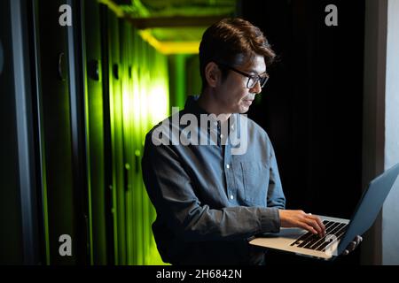 Asian male engineer using laptop in computer server room Stock Photo