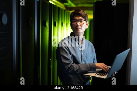 Asian male engineer using laptop in computer server room Stock Photo