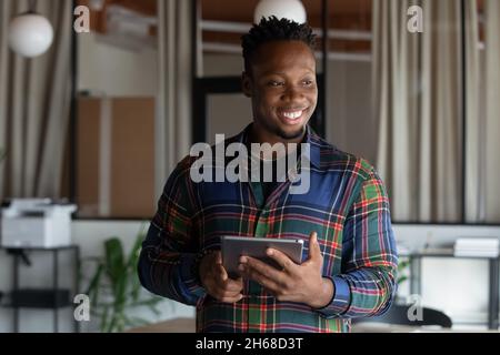 Joyful young dreamy african employee using digital tablet. Stock Photo