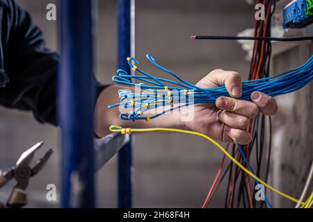 A male electrician works in a switchboard with an electrical connecting cable. Stock Photo