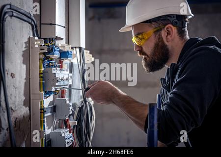 A male electrician works in a switchboard with an electrical connecting cable. Stock Photo