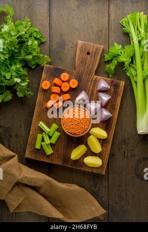 Vegetarian set of healthy vegetables on wooden board. Chopped carrots, potatoes, red onions, lentsils, parsley. Preparing ingredients for cooking soup Stock Photo