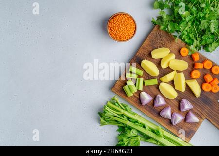 Vegetarian set of raw vegetables on wooden cutting board on light background. Chopped carrots, potatoes, red onions, lentsils, parsley. Preparing ingr Stock Photo