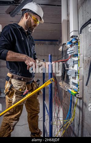 A male electrician works in a switchboard with an electrical connecting cable. Stock Photo