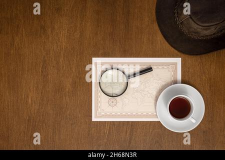 World map, magnifier and coffee on a wooden background, flat lay. Stock Photo