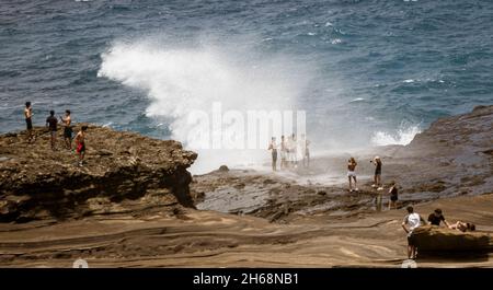 Honolulu, Hawaii - Nov 6, 2021-People stand on beach rocks as the surf goes over their heads. Stock Photo
