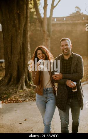 Handsome young couple walking in autumn park with coffee to go cups in hands Stock Photo