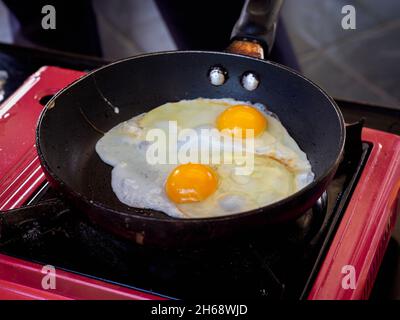 Twin fried egg in frying pan. Close up top view of the double fried eggs on a frying pan with red picnic gas stove. Stock Photo