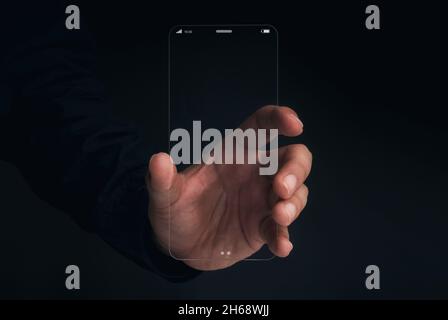 Futuristic transparent glass phone Technology. Super slim transparent future smartphone with vertical mock-up blank screen in hand on dark background. Stock Photo