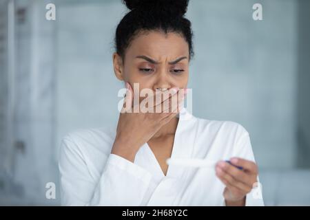 Stressed young african american woman looking at pregnancy test. Stock Photo