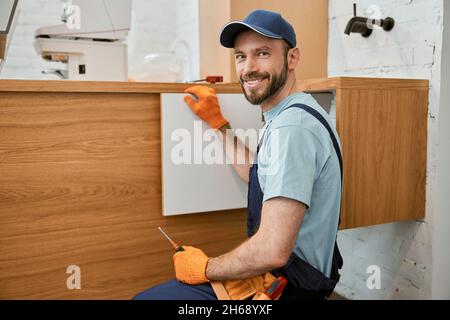 Cheerful male worker fixing cupboard door in kitchen Stock Photo