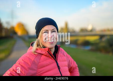 Middle-aged woman in beanie in an autumn landscape at sunset in a close up head and shoulders view as she is looking with a pensive smile Stock Photo