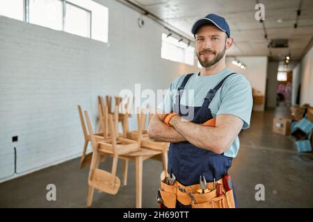 Cheerful male worker in cap standing in workshop Stock Photo