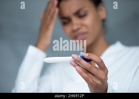 Unhappy frustrated young african ethnic woman holding pregnancy test. Stock Photo
