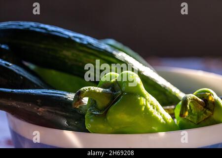 Fresh and washed green peppers and cucumbers in a bowl in the kitchen. Stock Photo