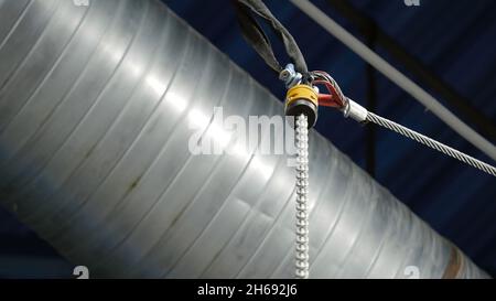 Bottom view of the suspension metal cable on th background of the ceiling and ventilation pipe. Technological details of the industrial room. Stock Photo