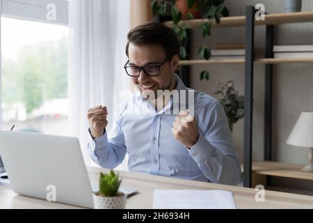 Happy young man in eyeglasses celebrating internet success. Stock Photo