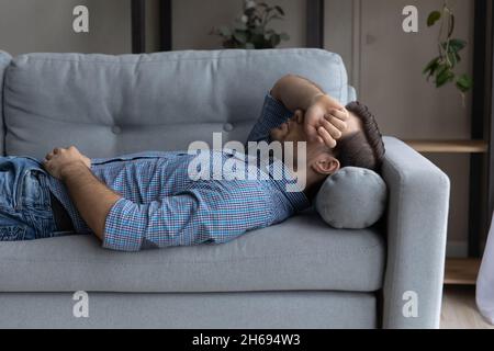 Stressed young man sleeping on sofa at home. Stock Photo