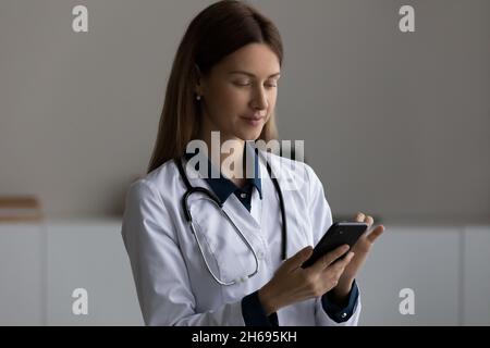 Head shot confident female doctor therapist in uniform using smartphone Stock Photo