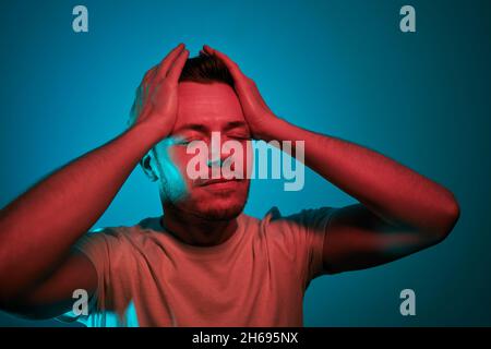 Portrait illuminated of neon lighting. Adult man in red and green lights have head in hands. Stock Photo