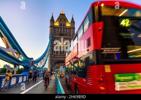 Red double decker bus crossing Tower Bridge at night, London, UK