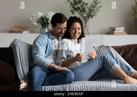 Happy couple hugging, using tablet together, relaxing on couch Stock Photo
