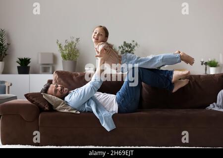 Laughing father lifting adorable daughter pretending flying, playing funny game Stock Photo