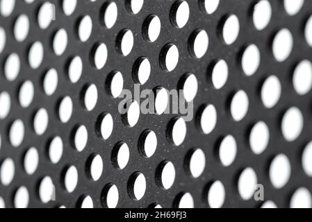 Macro shot of a black metal surface with round holes and white dots, isolated on a white background, selective focus. Stock Photo