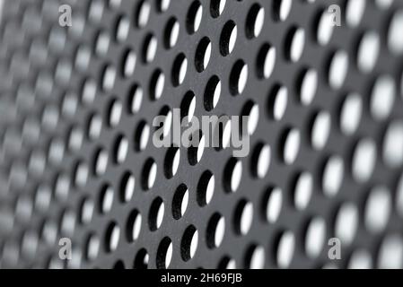 Macro shot of a black metal surface with round holes and white dots, isolated on a white background, selective focus. Stock Photo