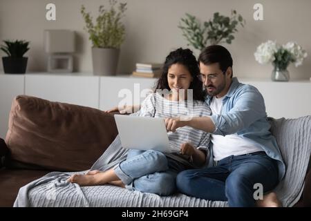 Happy young couple using laptop, relaxing sitting on couch together Stock Photo