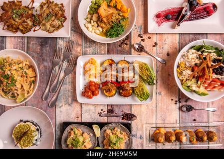 Top view image of vegan food dishes, boletus croquettes, poke bowl with wakame seaweed salad, edamame and pumpkin cubes, artichoke flowers, tacos with Stock Photo