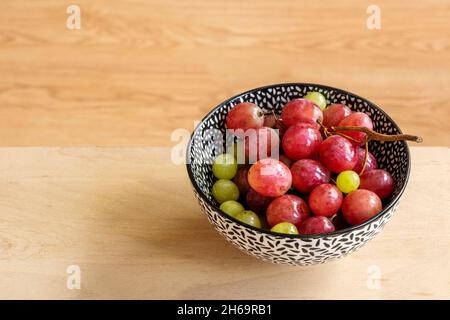 Bowl of freshly washed red and white grapes ready for breakfast on wooden table Stock Photo