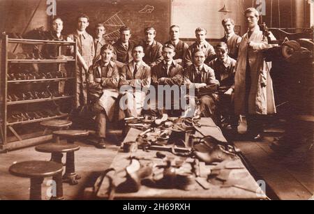 Group of cobblers or shoemakers photographed in their workshop. Tools and part completed shoes are on the worktable and finished boots and shoes are on a rack on one side, a blackboard with diagrams is on the back wall. Two of the men are wearing eye patches, possibly indicating that this is a group of ex-servicemen retraining after the First World War Stock Photo