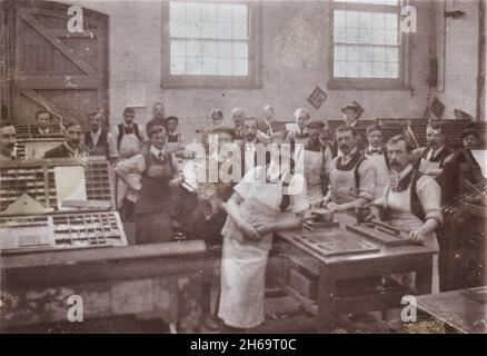 Printing workers posing in workshop, trays of movable type can be seen on the tables, early 20th century Stock Photo