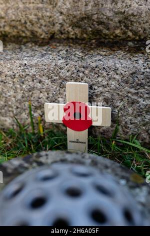 Remembrance Poppy on a wooden cross laid in front of a war memorial Stock Photo