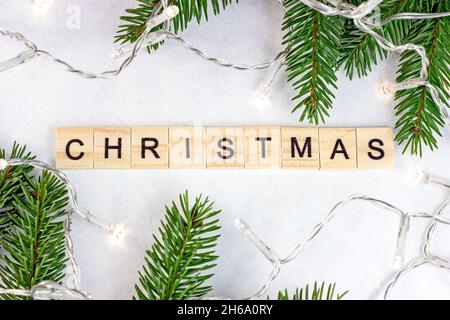 Top view of wooden Christmas text with green fir tree branches and lights as Xmas seasonal decoration on white background for greeting cards. Traditio Stock Photo