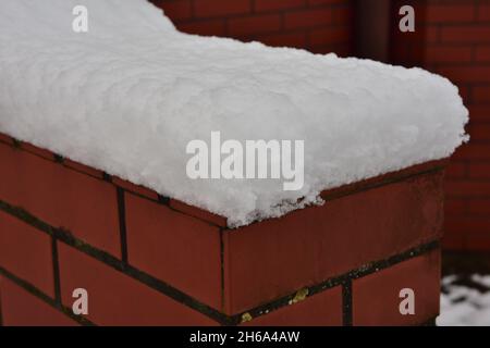 A brick wall of an unusual shape, covered with a snow cap. Stock Photo