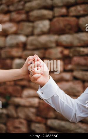 Man's hand with a ring on his finger holds woman's hand against the background of a stone fence. Close-up Stock Photo