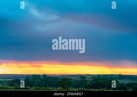 Dawn sky above the rural landscape in Kent. Dramatic sky, with heavy dark cumulus rain clouds and a narrow band of yellow sky on the horizon. Stock Photo