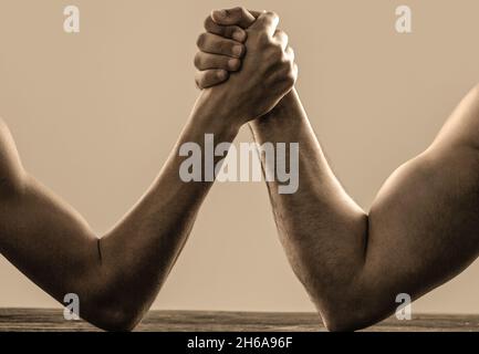 Arm wrestling. Heavily muscled man arm wrestling a puny weak man. Arms wrestling thin hand and a big strong arm in studio. Two man's hands clasped arm